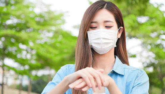 Woman rubbing hands with facemask on outside